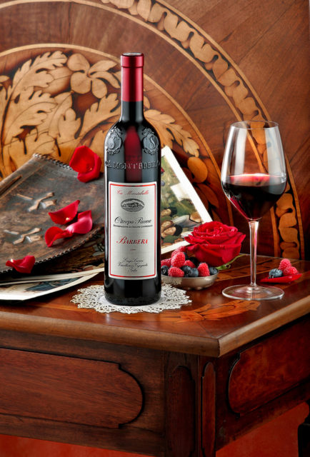 Foto still life del vino Barbera Scarani con bicchiere, rosa rossa, frutti di bosco, tavolino e fondo antico