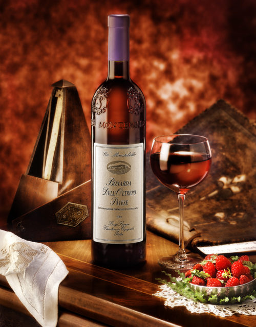 Foto still life del vino Bonarda con bicchiere,lamponi, metronomo, spartito e fondo anticato