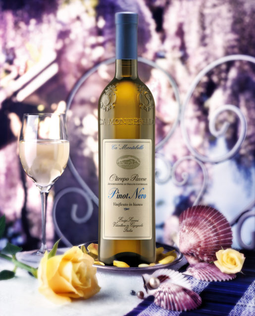 Foto still life del vino Pinot Nero vinificato Bianco Scarani con bicchiere, rosa gialla,capasanta,sfondo glicine