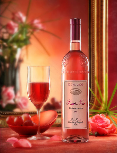 Foto still life del vino Pinot Nero Vinificato rosato con bicchiere, acini d'uva, rosa e fondo con specchio